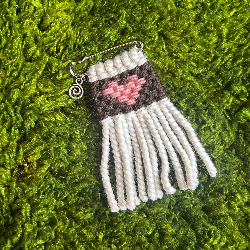 Woven heart  pin on a textured green moss background