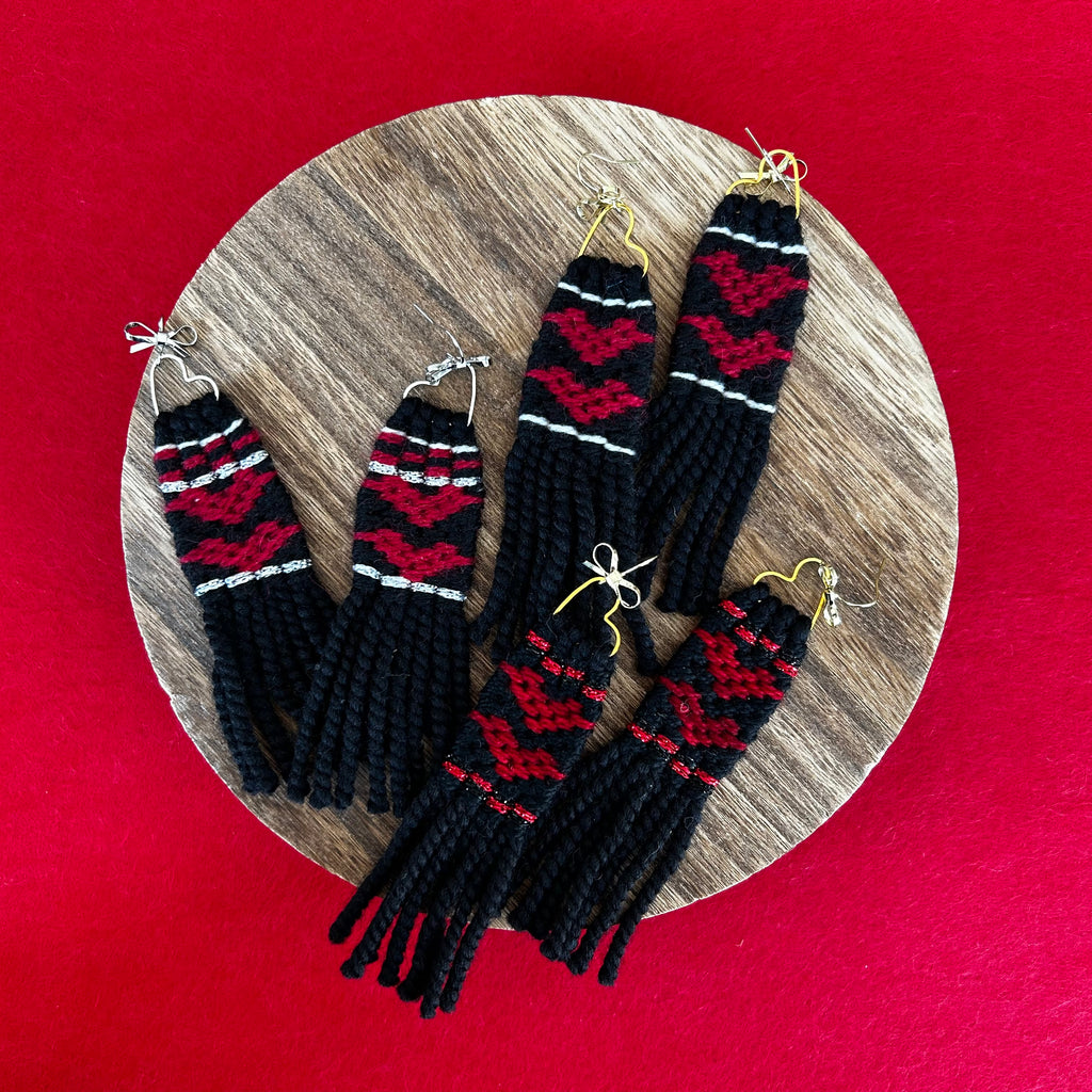 Black and red patterned earrings on a wooden stand with a red background