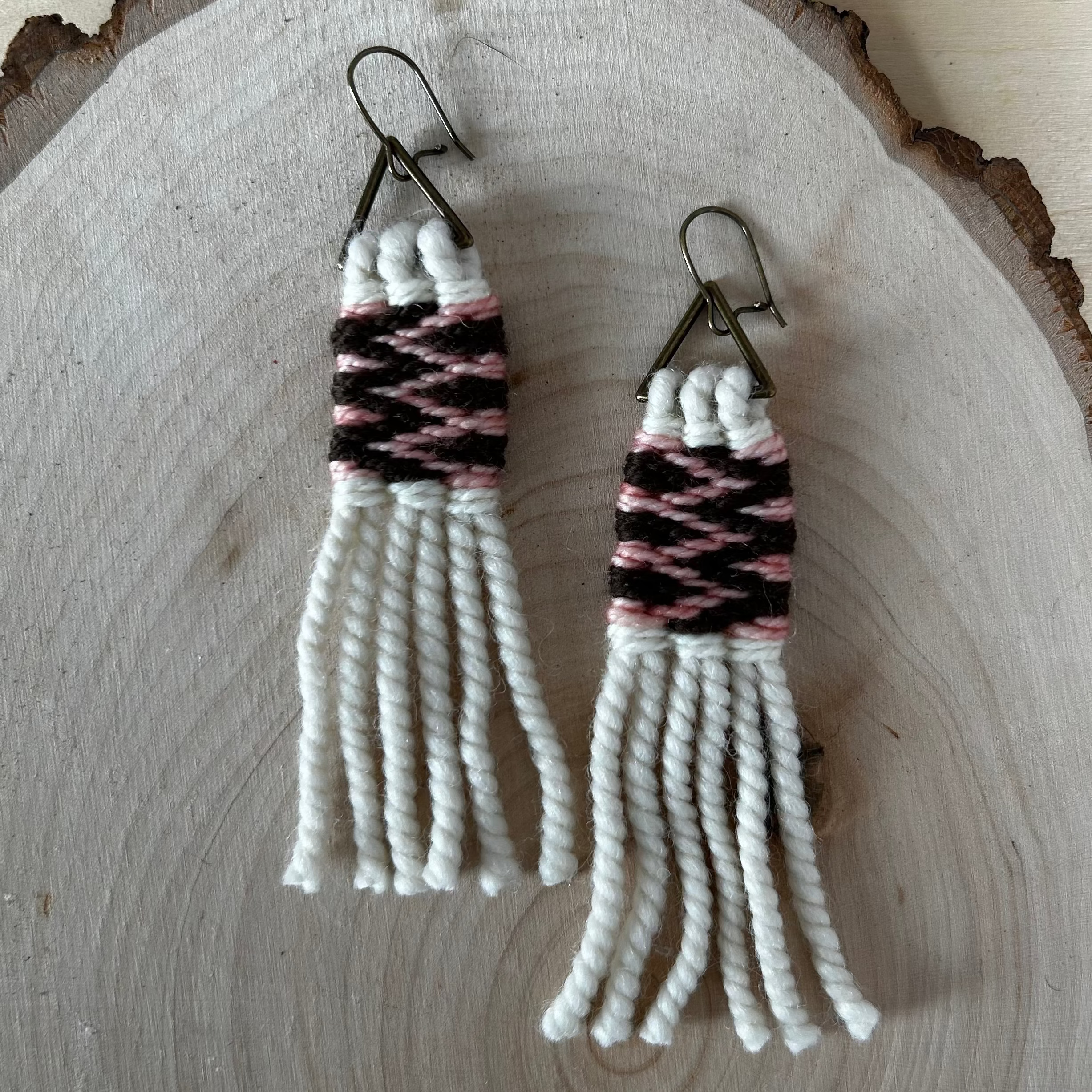 Pair of woven earrings with white and pink pattern on a wooden surface