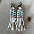 Woven yarn sage green and cream earrings on a wooden surface