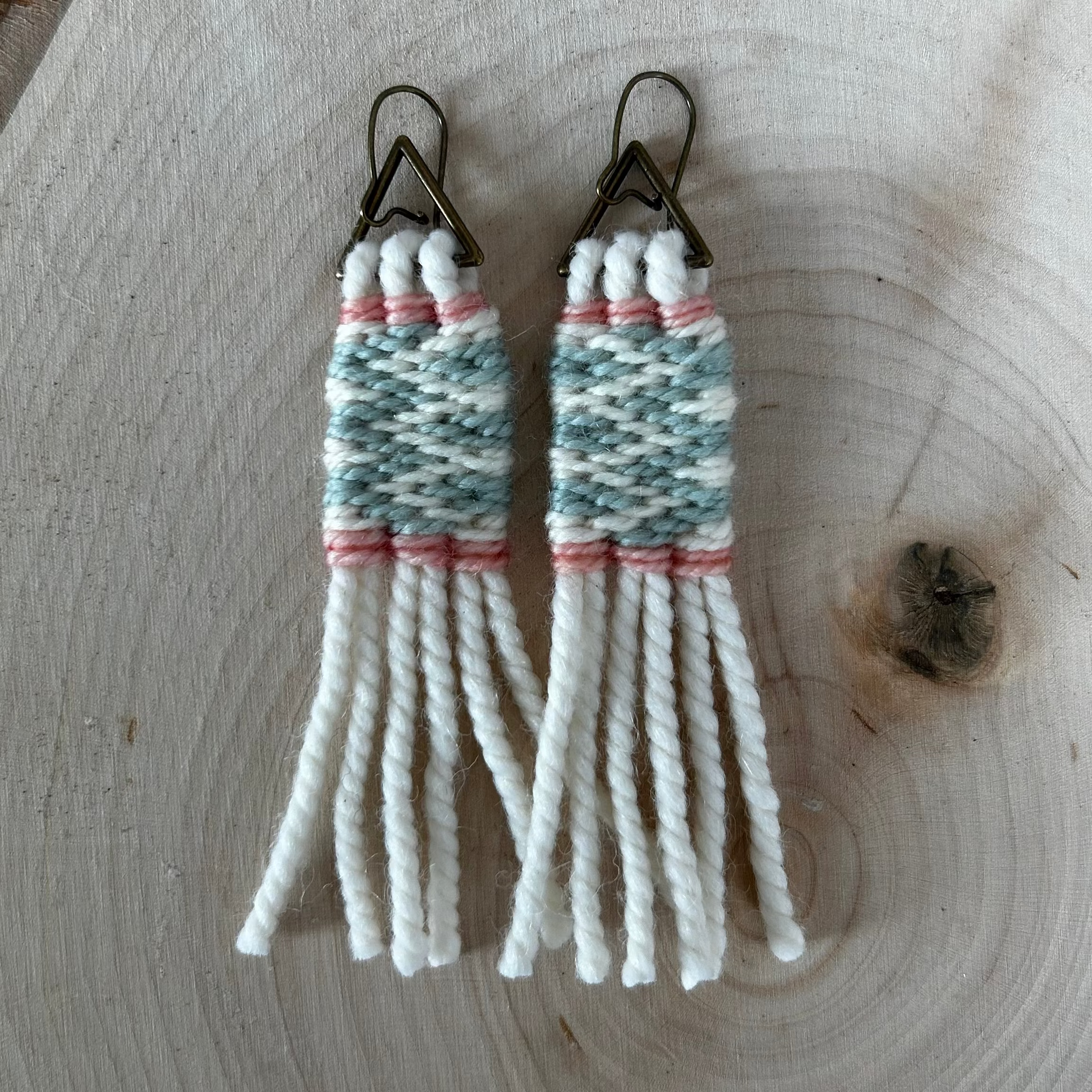 Woven yarn sage green and cream earrings on a wooden surface