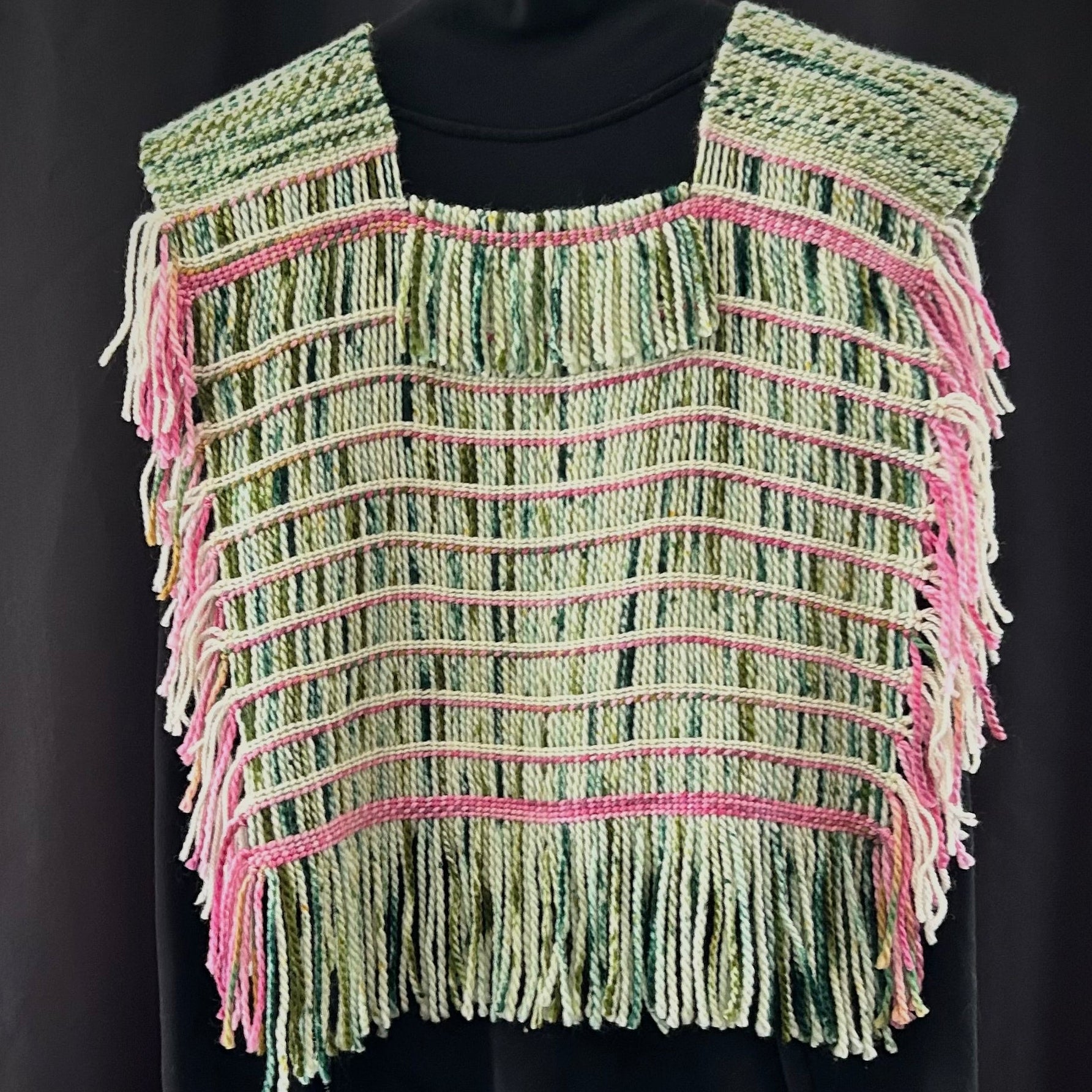 Green and pink woven vest on a black mannequin against a dark background